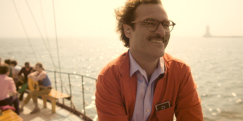 Joaquin Phoenix nei panni di Theodore, in camicia rossa, sorride su una barca alla luce del sole